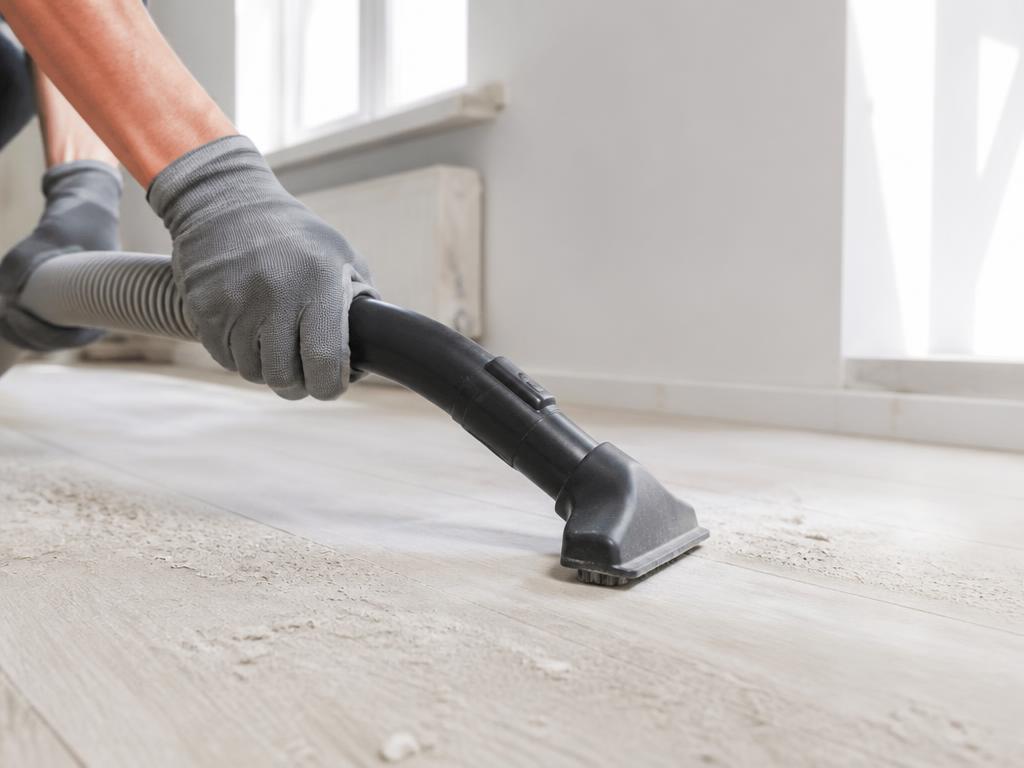 Gloved hands vacuuming construction dust from a new floor